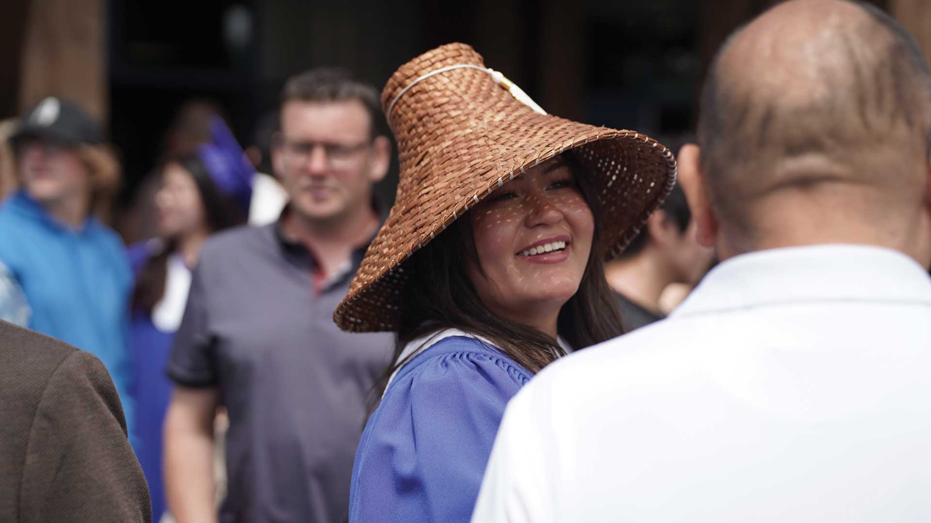 NIC alum at convocation wearing a woven cedar hat and graduate regalia