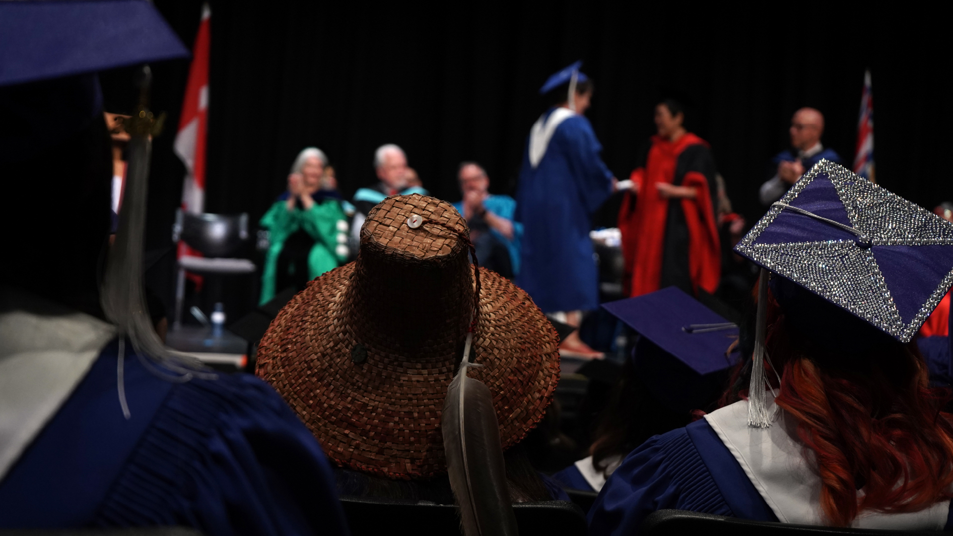 graduates watch from the audience as a classmate crosses the stage