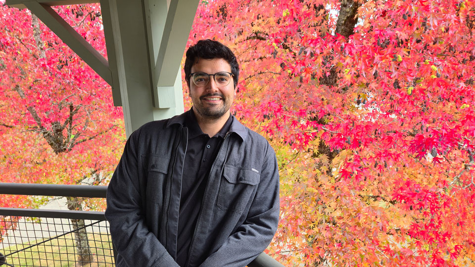 A former student stands by trees in fall near his former college