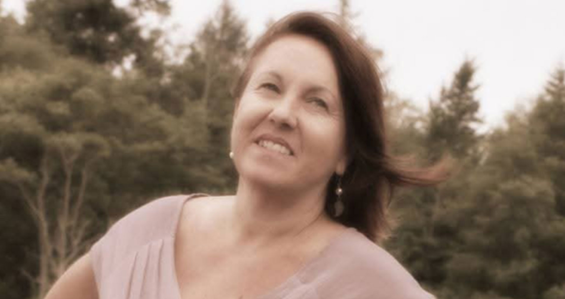A woman stands in front of trees