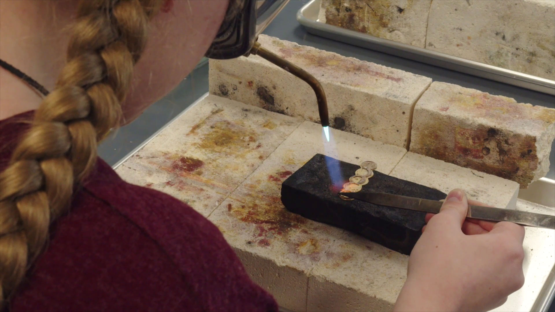 Metal jewellery student using a torch to construct a brooch