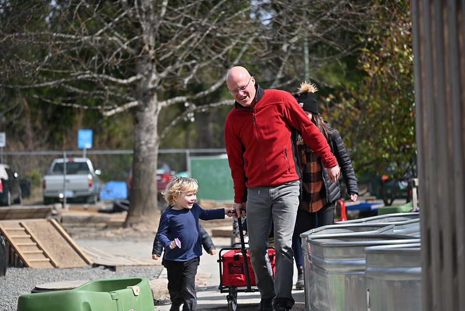 Child smiles while pulling wagon with educator in outdoor play area